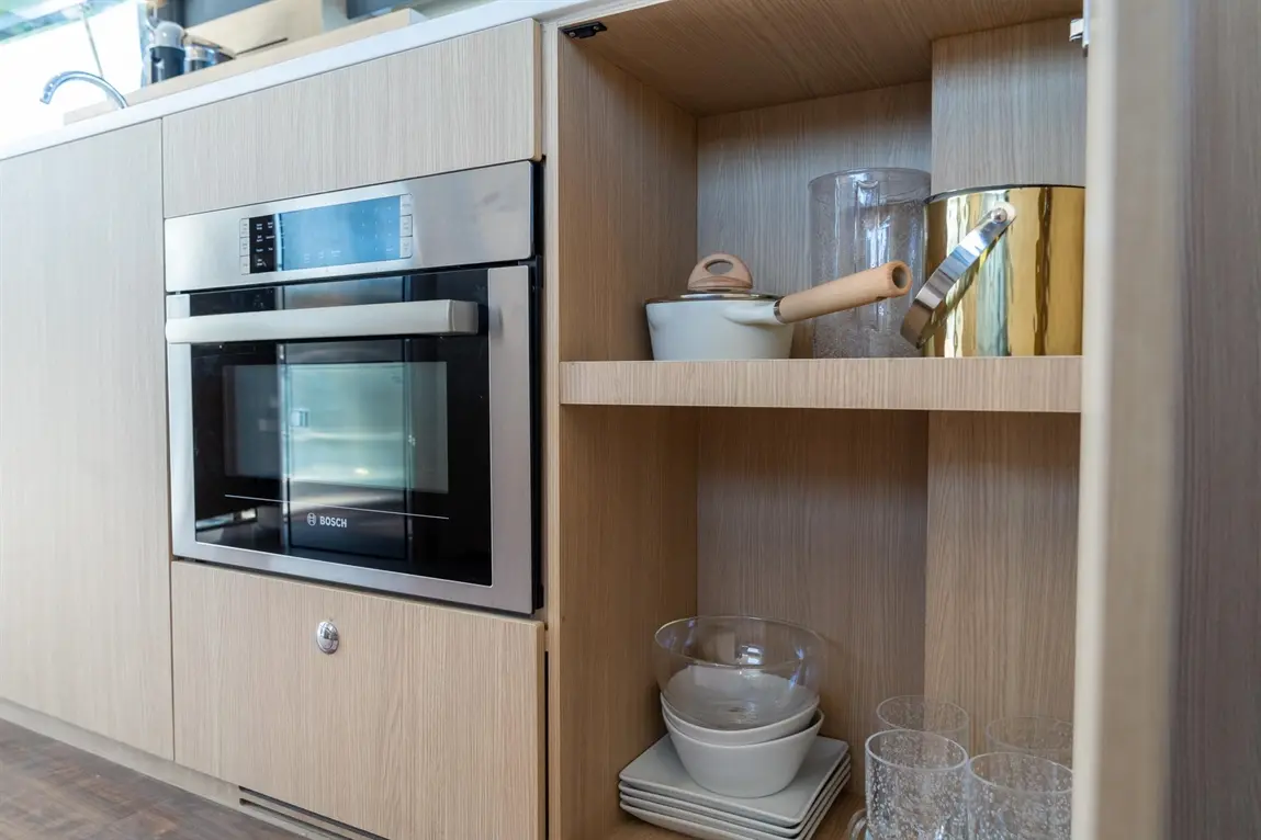 Modern kitchen cabinet showcasing a Bosch oven, glassware, plates, and a saucepan on wooden shelves against a stylish backdrop.